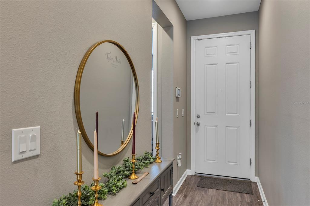 An entryway features a gray console table, a round gold mirror, and a white front door — 2012 SLOANS OUTLOOK DRIVE, GROVELAND, FL