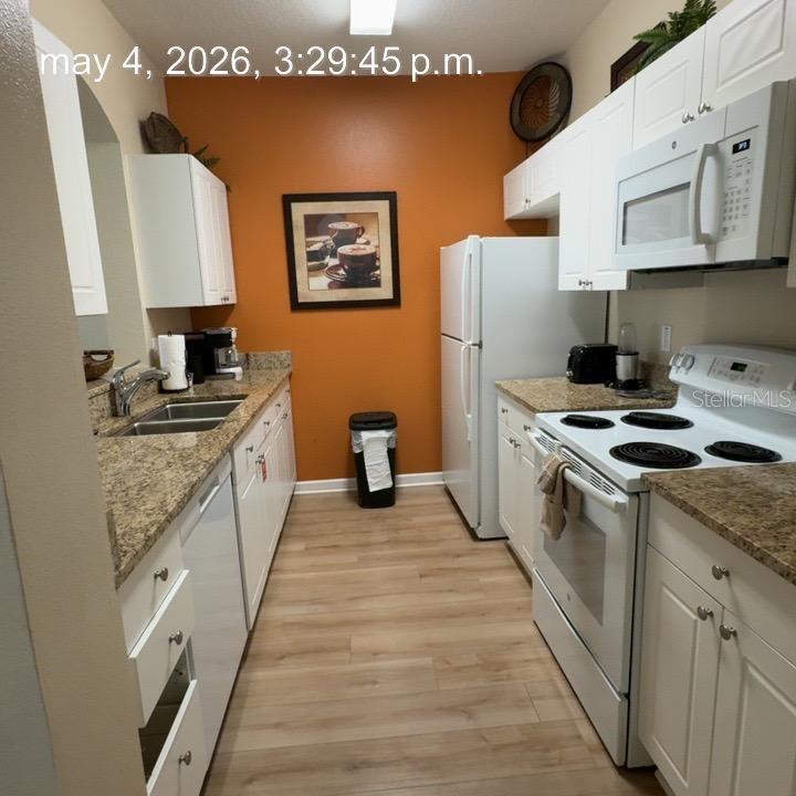 A galley kitchen features white cabinets, granite countertops, white appliances, and an orange accent wall — 8107 COCONUT PALM WAY UNIT 201, KISSIMMEE, FL