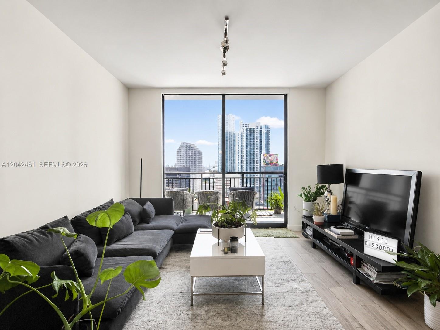 A living room features a dark sectional sofa, white coffee table, and balcony with city views — 999 SW 1st Ave # 2211, Miami FL 33130, MIAMI, FL
