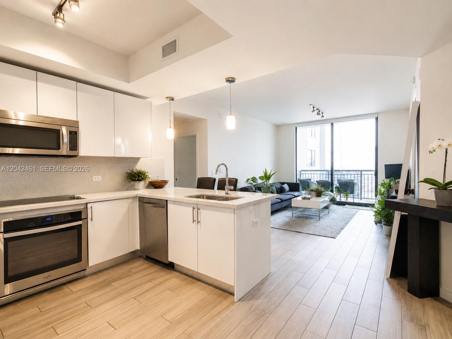 A modern kitchen with white cabinets and stainless steel appliances opens into a living area — 999 SW 1st Ave # 2211, Miami FL 33130, MIAMI, FL