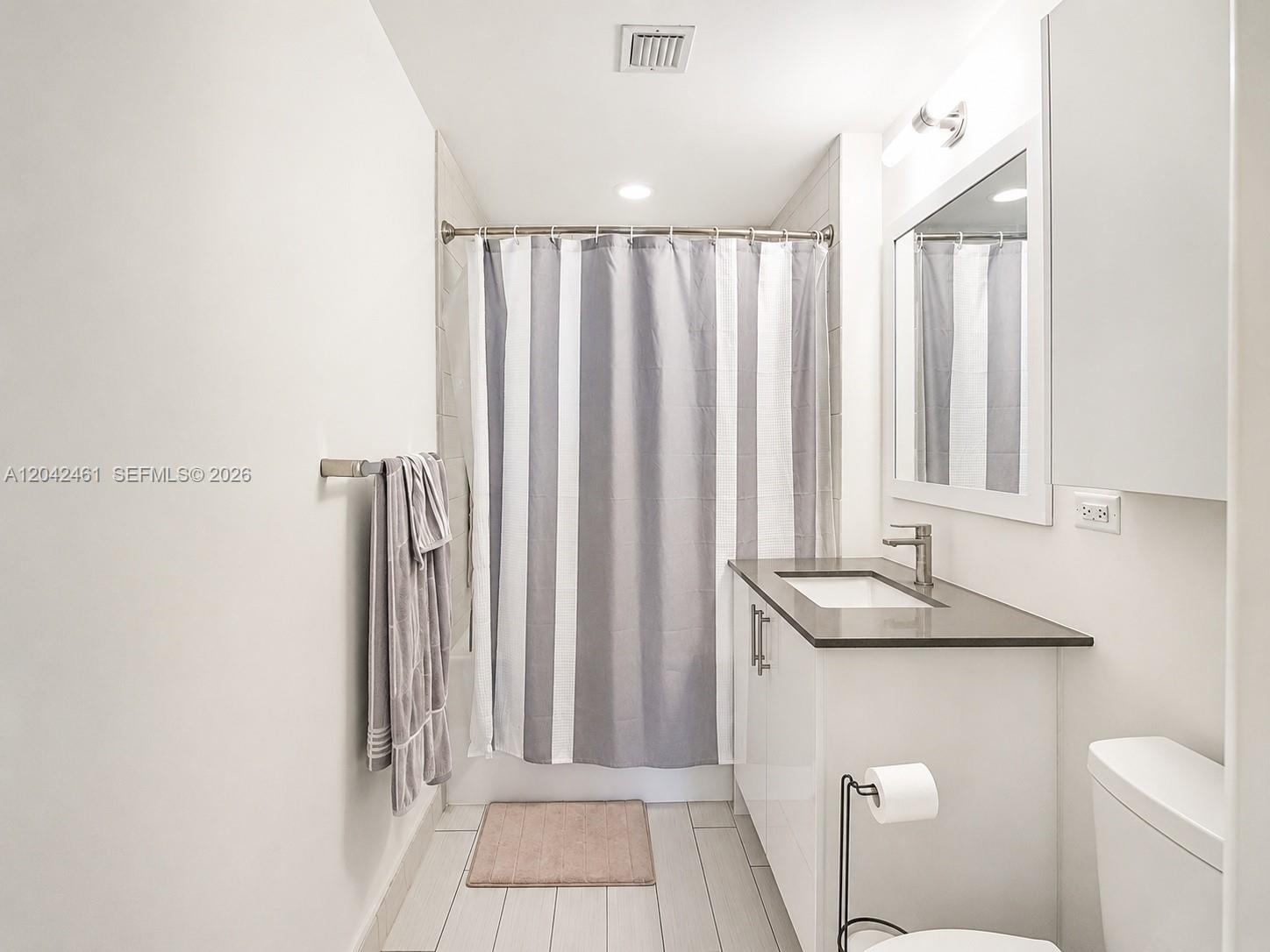 A modern bathroom features a white vanity, a gray-striped shower curtain, and light-colored tile flooring — 999 SW 1st Ave # 2211, Miami FL 33130, MIAMI, FL
