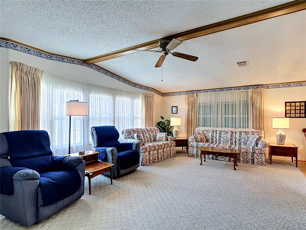 A living room features floral sofas, blue recliners, a ceiling fan, and wall-to-wall carpeting — 35801 BRISA DRIVE, ZEPHYRHILLS, FL