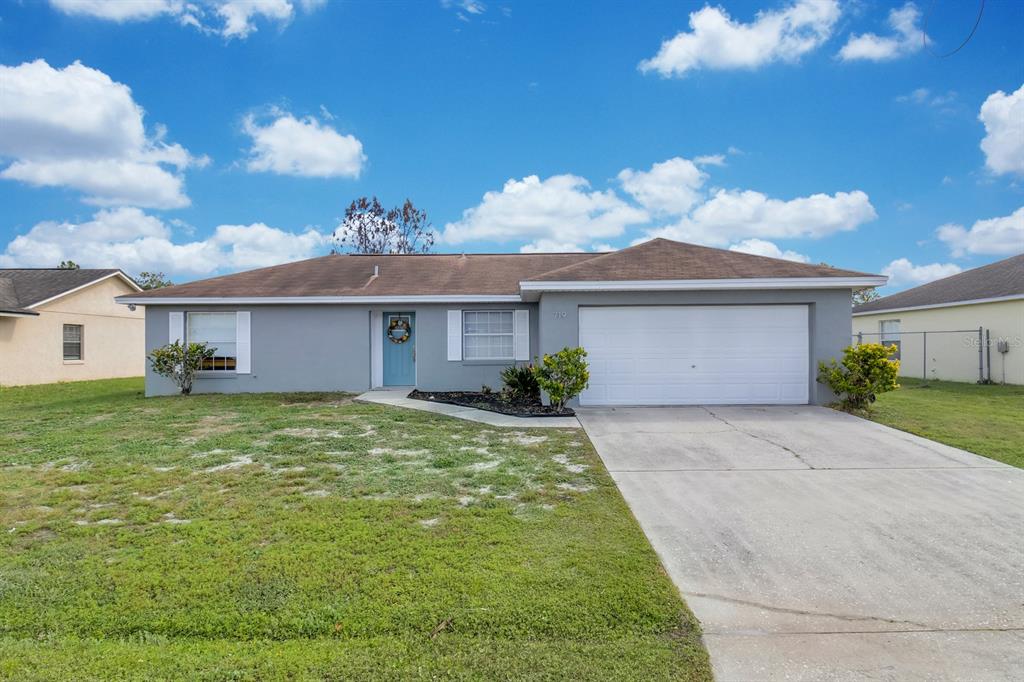 A single-story gray house with a white garage door, blue front door, and grassy lawn — 719 DEL RAY DRIVE, KISSIMMEE, FL