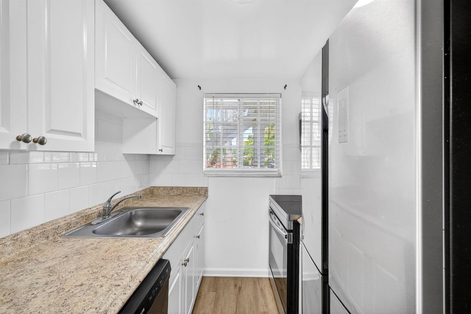 A galley kitchen features white cabinets, granite countertops, a stainless steel sink, and white appliances — 3380 NE 16th Terrace Unit 3, Pompano Beach FL 33064, POMPANO BEACH, FL