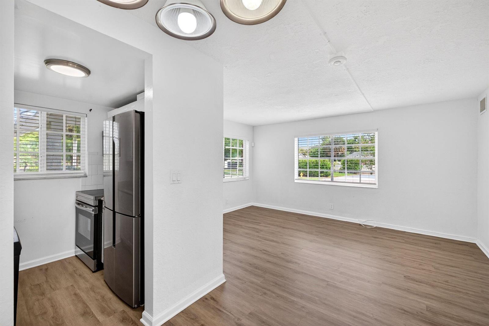 A kitchen with stainless steel appliances opens into a bright living area with wood flooring — 3380 NE 16th Terrace Unit 3, Pompano Beach FL 33064, POMPANO BEACH, FL