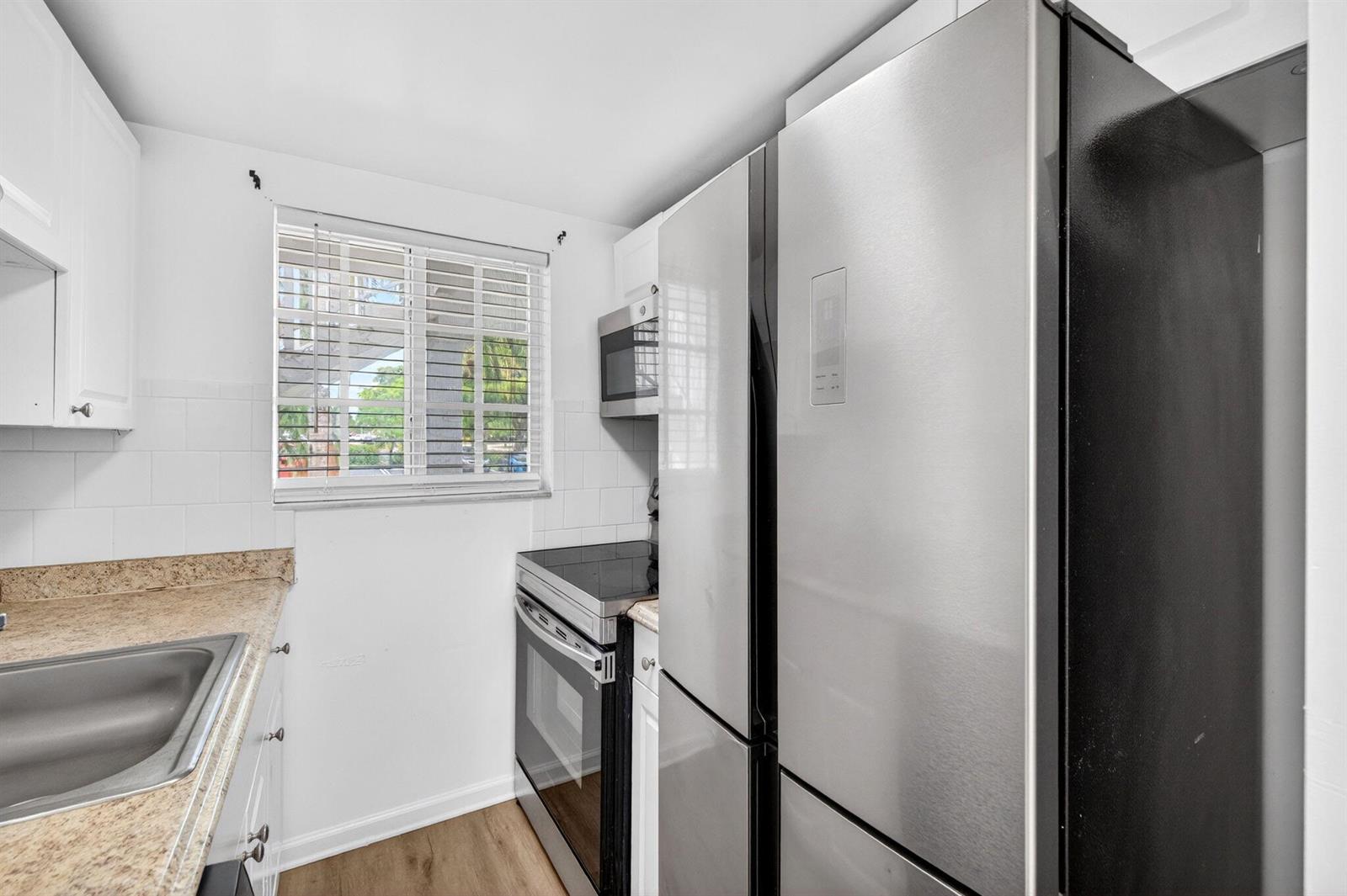 A kitchen features stainless steel appliances, white cabinets, a window, and tan countertops — 3380 NE 16th Terrace Unit 3, Pompano Beach FL 33064, POMPANO BEACH, FL