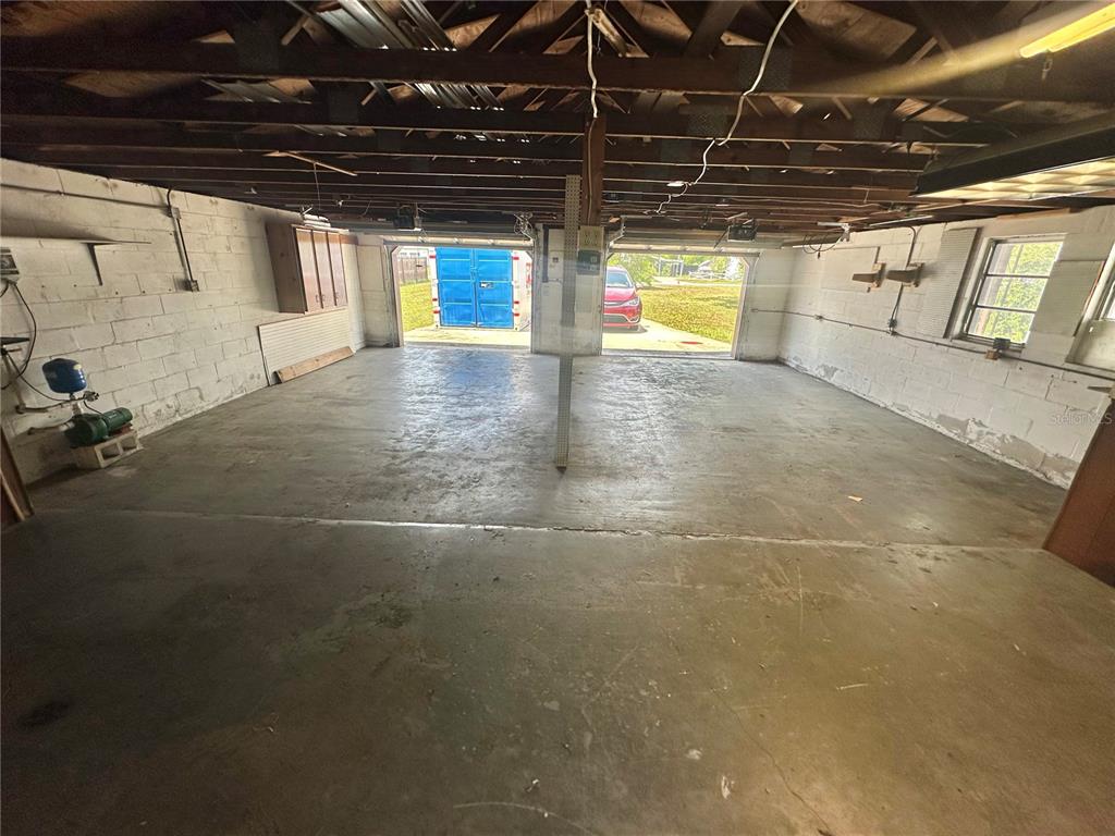 An unfinished two-car garage features exposed ceiling joists, concrete floors, and white block walls — 9702 ANDY DRIVE, HUDSON, FL