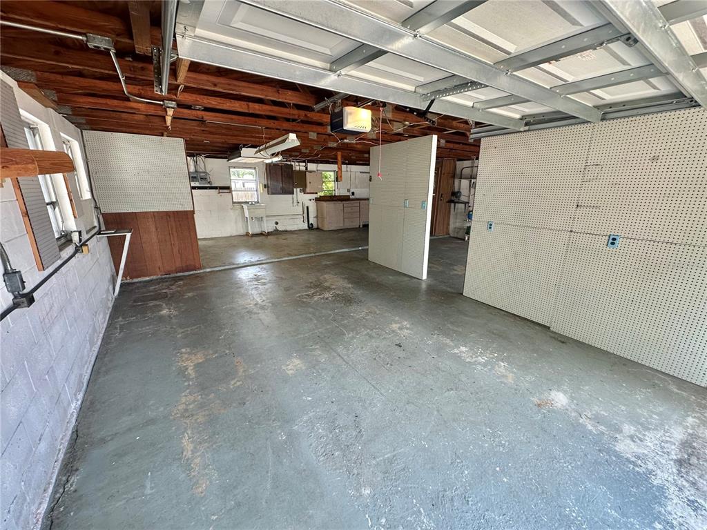 An interior view of a garage with a concrete floor, pegboard walls, and exposed ceiling joists — 9702 ANDY DRIVE, HUDSON, FL