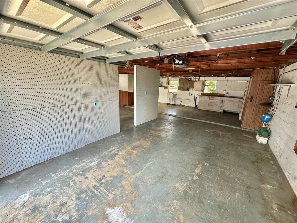 A garage interior features a concrete floor, pegboard walls, exposed ceiling joists, and a workbench — 9702 ANDY DRIVE, HUDSON, FL