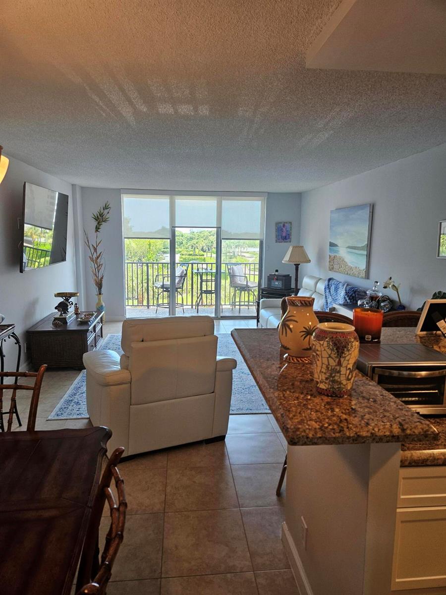 A living room with a white armchair, granite kitchen counter, and a balcony overlooking greenery — 2121 N Ocean Boulevard N # 405e, Boca Raton FL 33431, BOCA RATON, FL