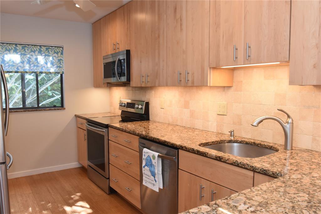 A kitchen features light wood cabinets, granite countertops, stainless steel appliances, and a tiled backsplash — 1601 BAYHOUSE POINT DRIVE UNIT BA201, SARASOTA, FL