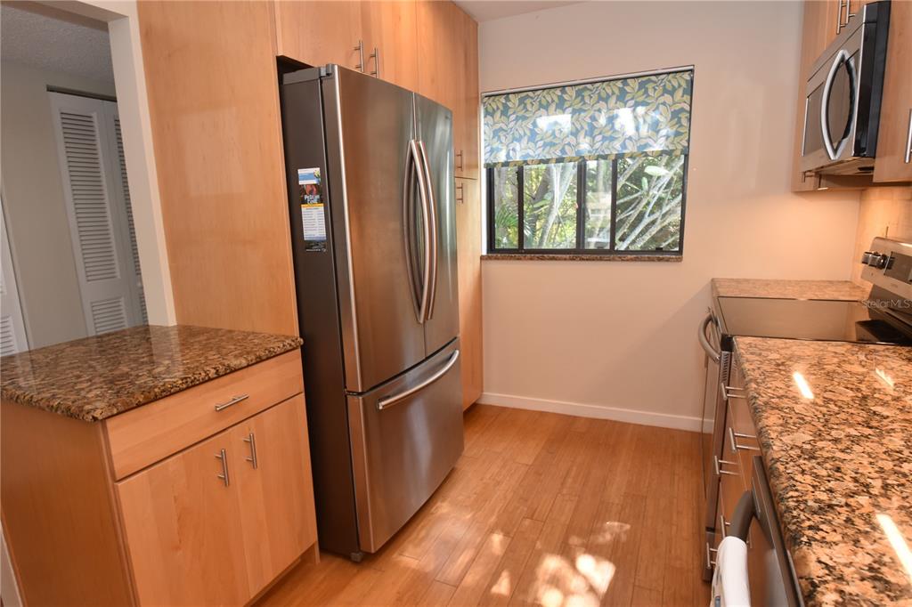A kitchen features light wood cabinets, granite countertops, stainless steel appliances, and wood flooring — 1601 BAYHOUSE POINT DRIVE UNIT BA201, SARASOTA, FL