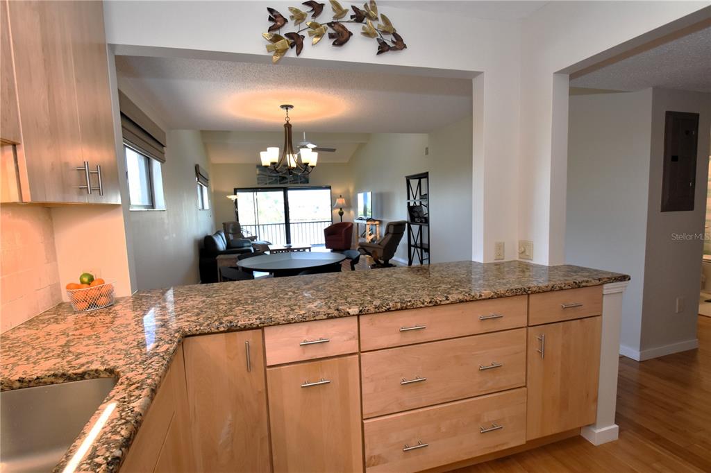 A kitchen with light wood cabinets and granite countertops overlooks an open-concept living area — 1601 BAYHOUSE POINT DRIVE UNIT BA201, SARASOTA, FL