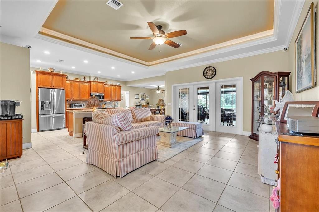 An open-concept living room and kitchen featuring tile flooring, a tray ceiling, and striped furniture — 11614 SW COURTLY MANOR DRIVE, LAKE SUZY, FL