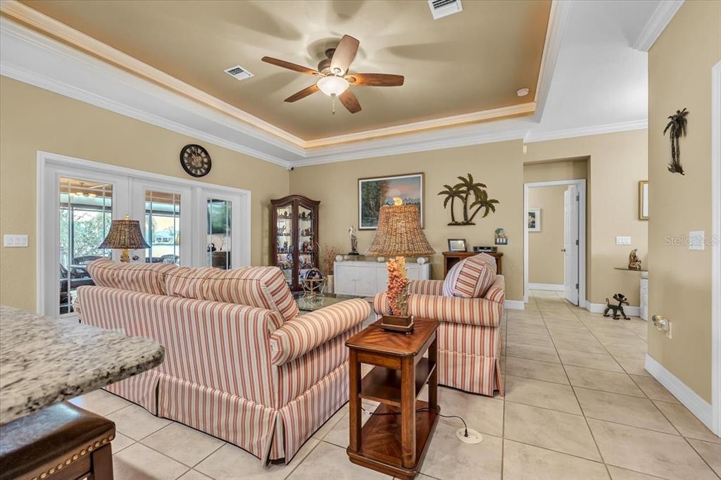 A living room features striped sofas, a ceiling fan, and tile flooring — 11614 SW COURTLY MANOR DRIVE, LAKE SUZY, FL