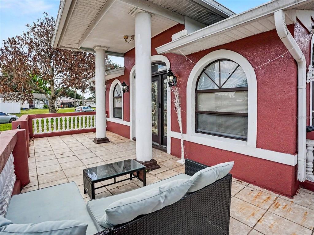 A red stucco porch features white columns, arched windows, and tiled flooring with outdoor furniture — 151 TULPAN DRIVE, KISSIMMEE, FL