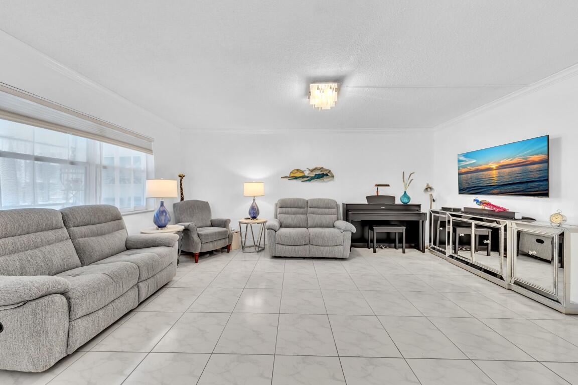 A living room features gray upholstered furniture, a piano, and a mirrored media console — 580 Egret Drive # 121, Hallandale Beach FL 33009, HALLANDALE BEACH, FL