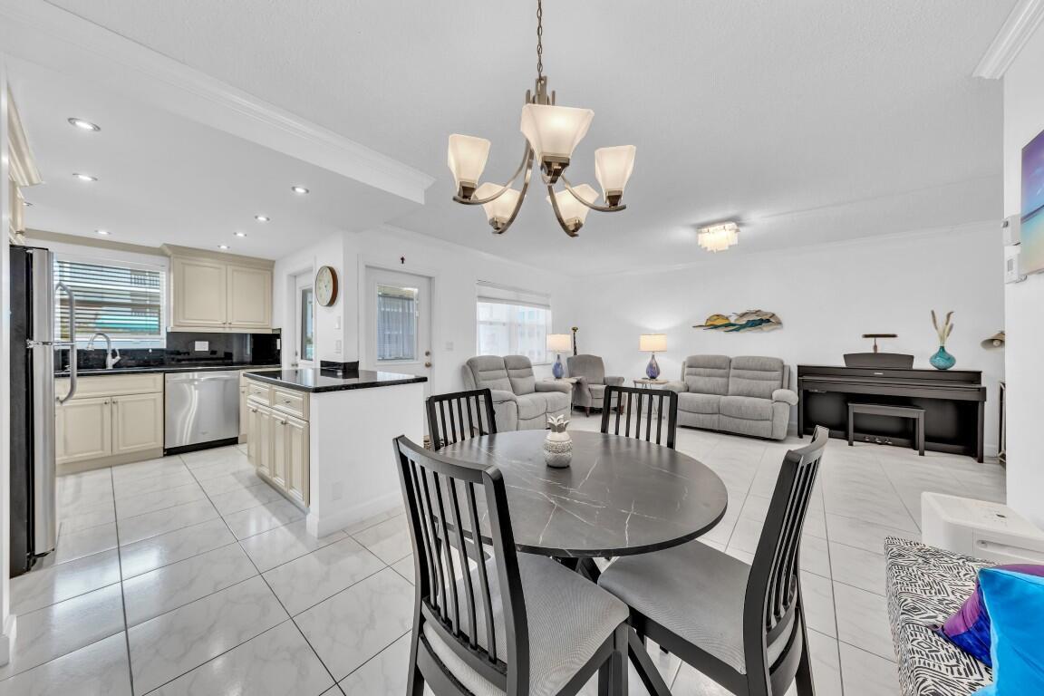 An open-concept kitchen and dining area features white cabinets, tile flooring, and a chandelier — 580 Egret Drive # 121, Hallandale Beach FL 33009, HALLANDALE BEACH, FL