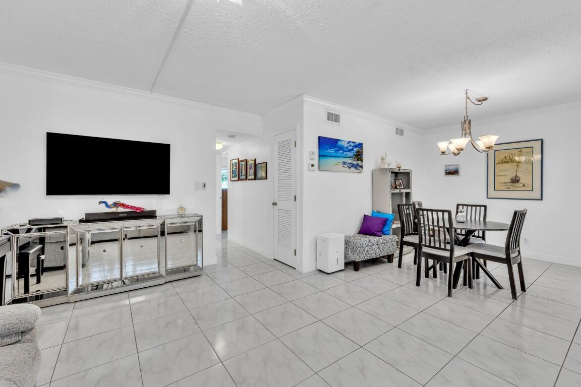 A bright living and dining area with white tile floors, a mirrored console, and furniture — 580 Egret Drive # 121, Hallandale Beach FL 33009, HALLANDALE BEACH, FL