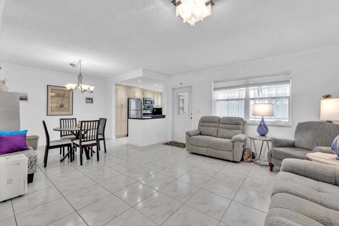 An open-concept living and dining area features white tile floors and neutral furniture — 580 Egret Drive # 121, Hallandale Beach FL 33009, HALLANDALE BEACH, FL