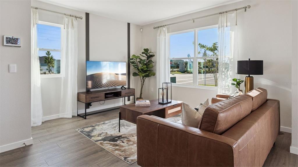 A living room features a brown leather sofa, wood-look flooring, and a television on a stand — 284 PRESTON COVE DRIVE, ST CLOUD, FL
