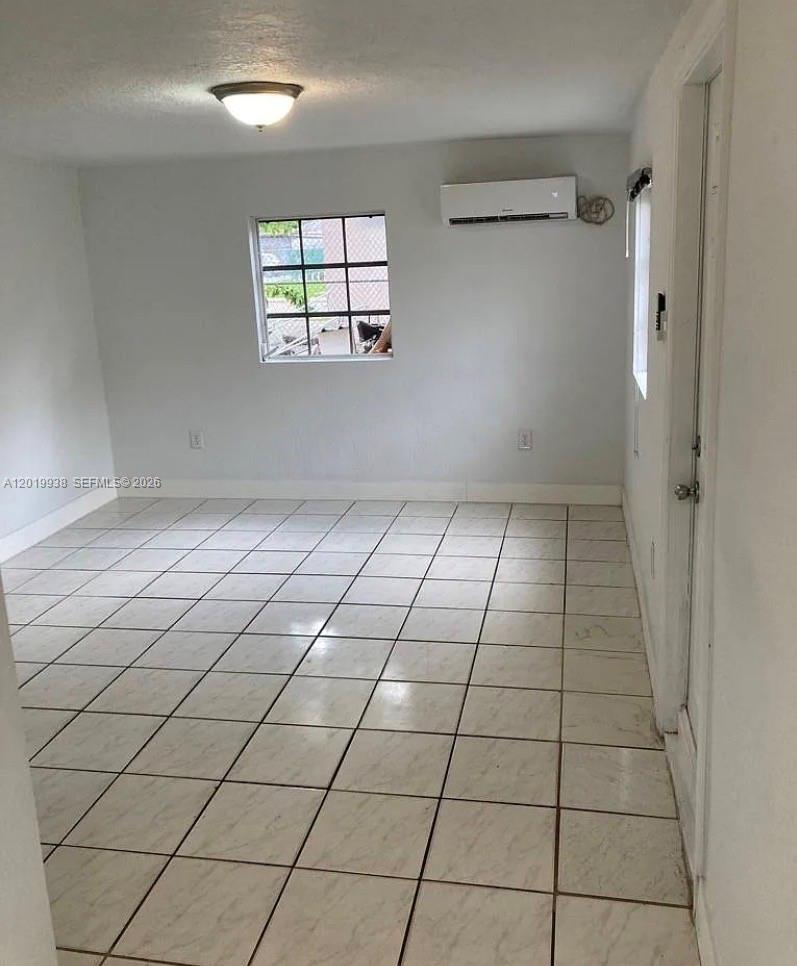 A room with light-colored walls, tiled flooring, a window with security bars, and a wall-mounted AC — 141 W 26th St, Hialeah FL 33010, HIALEAH, FL