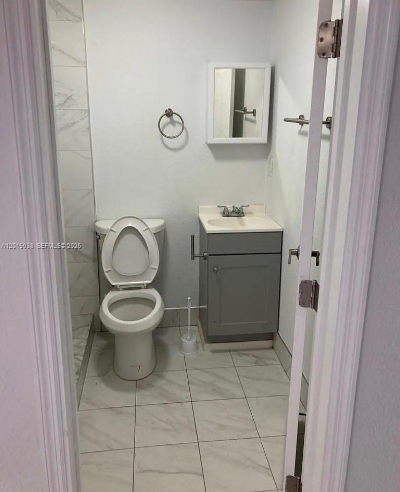 A small bathroom features a white toilet, a gray vanity, and light-colored tile flooring — 141 W 26th St, Hialeah FL 33010, HIALEAH, FL
