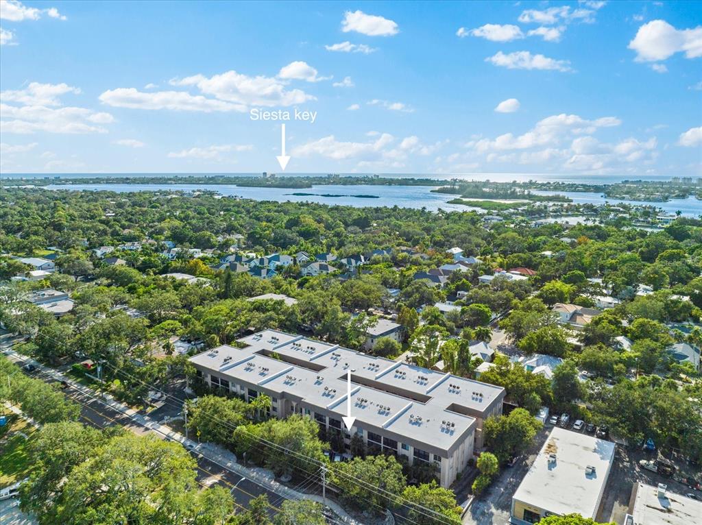 An aerial view shows a multi-story apartment building surrounded by trees near a coastal waterway — 3700 S OSPREY AVENUE UNIT 214, SARASOTA, FL