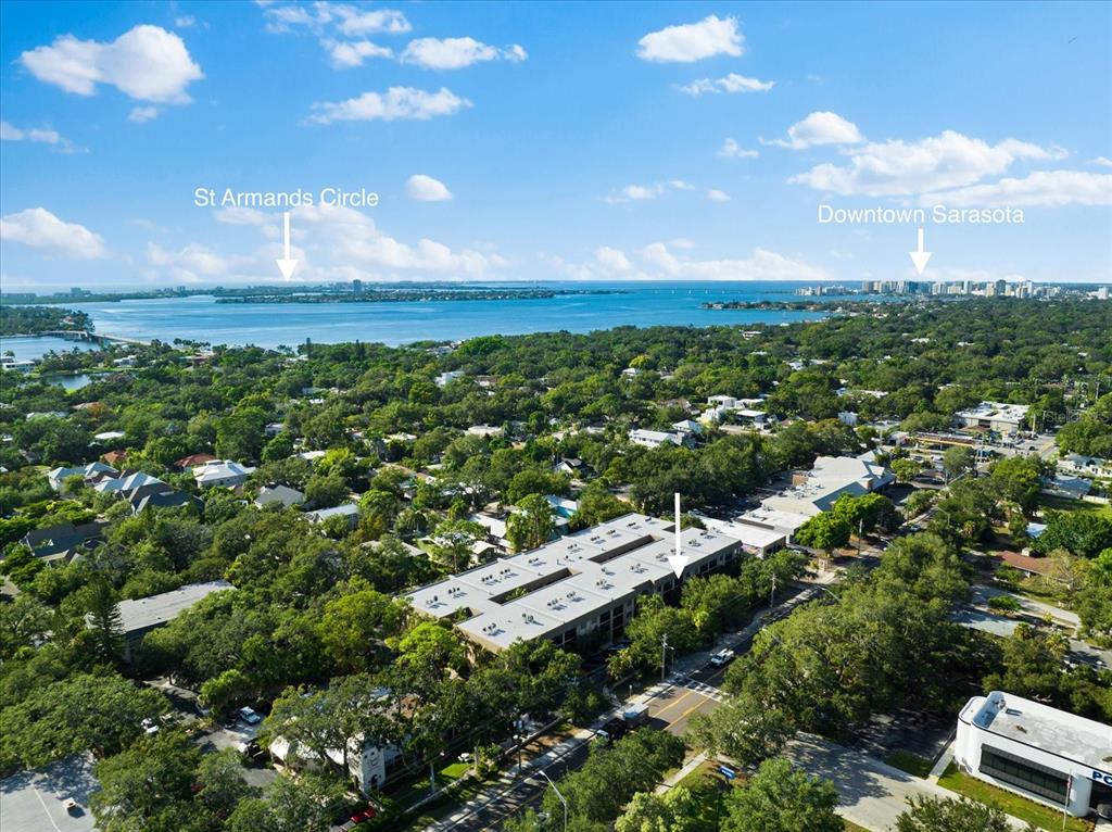 An aerial view shows a multi-story building surrounded by trees with distant water and city views — 3700 S OSPREY AVENUE UNIT 214, SARASOTA, FL
