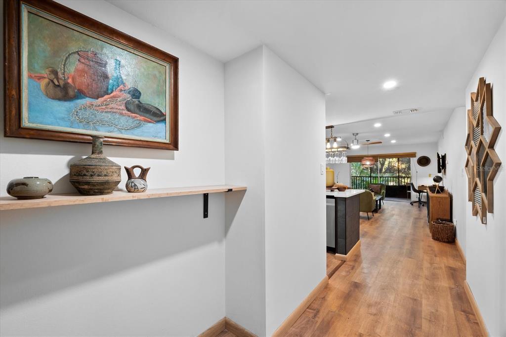 A hallway with a wooden shelf and wall art leads into an open-concept living area — 3700 S OSPREY AVENUE UNIT 214, SARASOTA, FL
