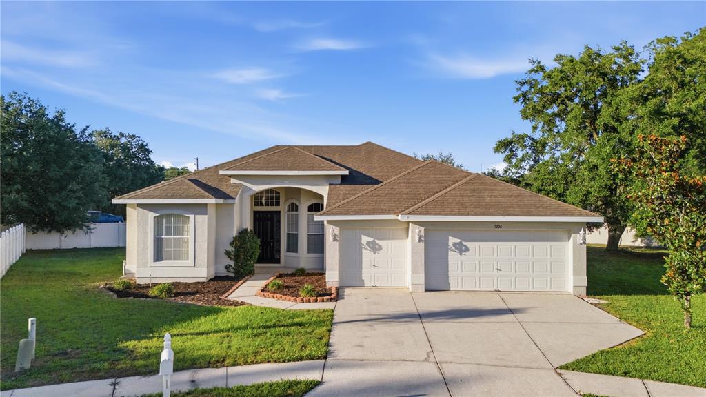 A single-story house with a beige stucco exterior, a brown shingled roof, and a driveway — 7006 ORVICTI COURT, WESLEY CHAPEL, FL