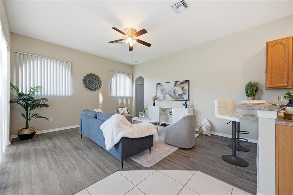 A living room features gray wood-look flooring, a blue sofa, two armchairs, and a breakfast bar — 7006 ORVICTI COURT, WESLEY CHAPEL, FL