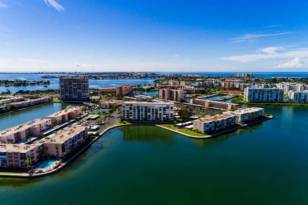An aerial view shows multiple waterfront apartment complexes surrounded by a bay under a blue sky — 7700 SUN ISLAND DRIVE S UNIT 608, SOUTH PASADENA, FL