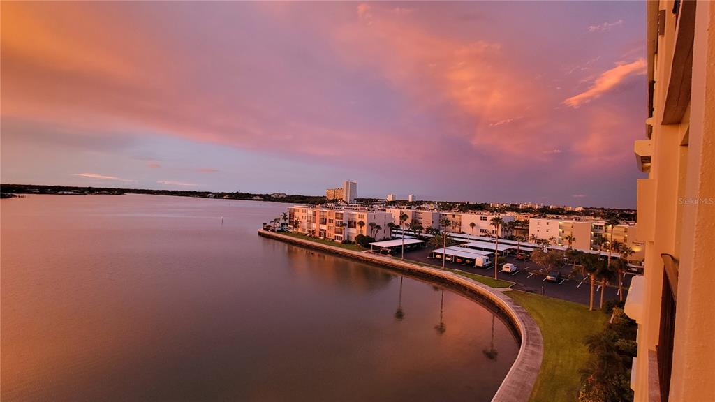 An elevated view of a waterfront apartment complex at sunset with a parking lot below — 7700 SUN ISLAND DRIVE S UNIT 608, SOUTH PASADENA, FL