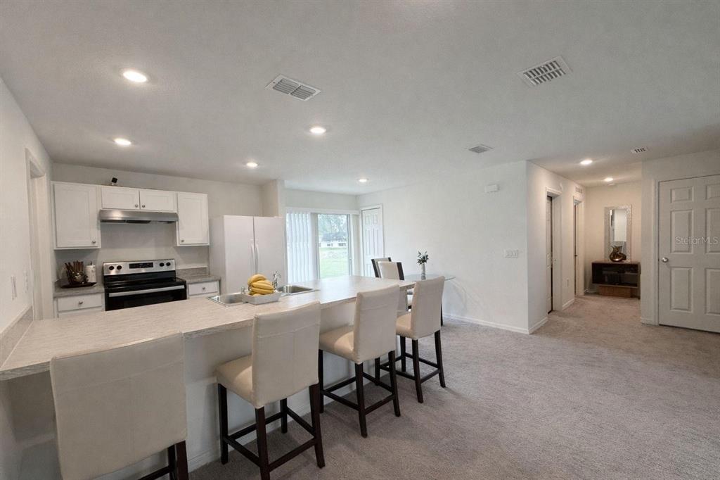 A kitchen with white cabinets and a breakfast bar overlooks an open carpeted living area — 17103 SW 22ND TERRACE ROAD, OCALA, FL