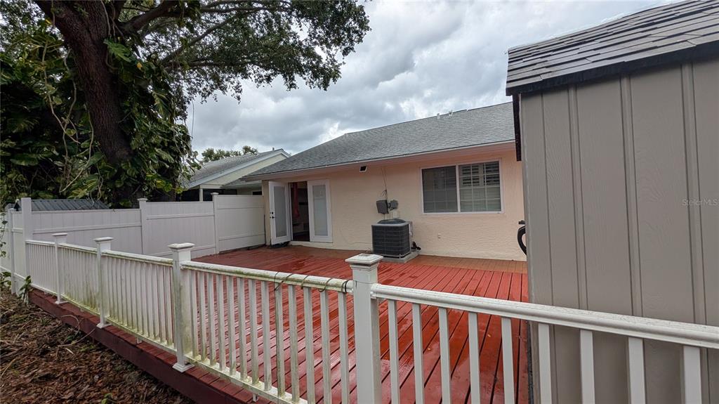 A backyard features a red wooden deck, a white vinyl fence, and a storage shed — 4000 POINCIANA COURT, PALM HARBOR, FL
