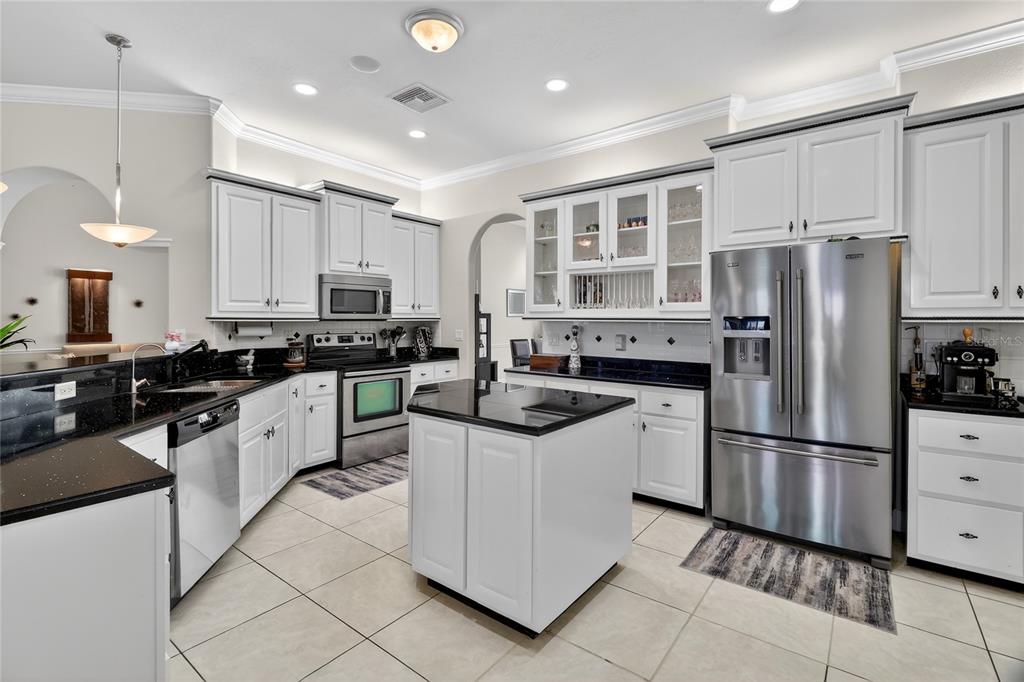 A kitchen features white cabinets, black countertops, stainless steel appliances, and a central island — 1028 S LAKE MARIAM DRIVE, WINTER HAVEN, FL
