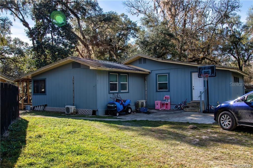 A blue single-story house with a concrete driveway, a basketball hoop, and surrounding trees — 7545 S OLD OAKS DRIVE, FLORAL CITY, FL