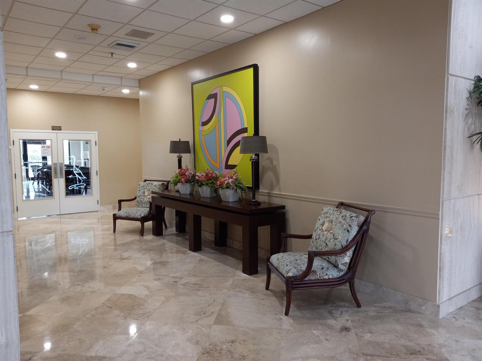 A lobby features a console table with lamps and flowers beneath abstract art and chairs — 9960 S Ocean Drive # 502, Jensen Beach FL 34957, JENSEN BEACH, FL