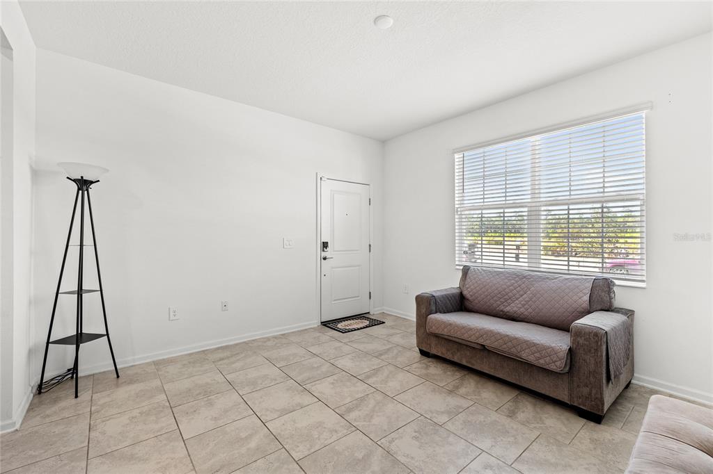 A living room with tile flooring, a gray sofa, a floor lamp, and a front door — 3075 CAMDEN WAY, DAVENPORT, FL