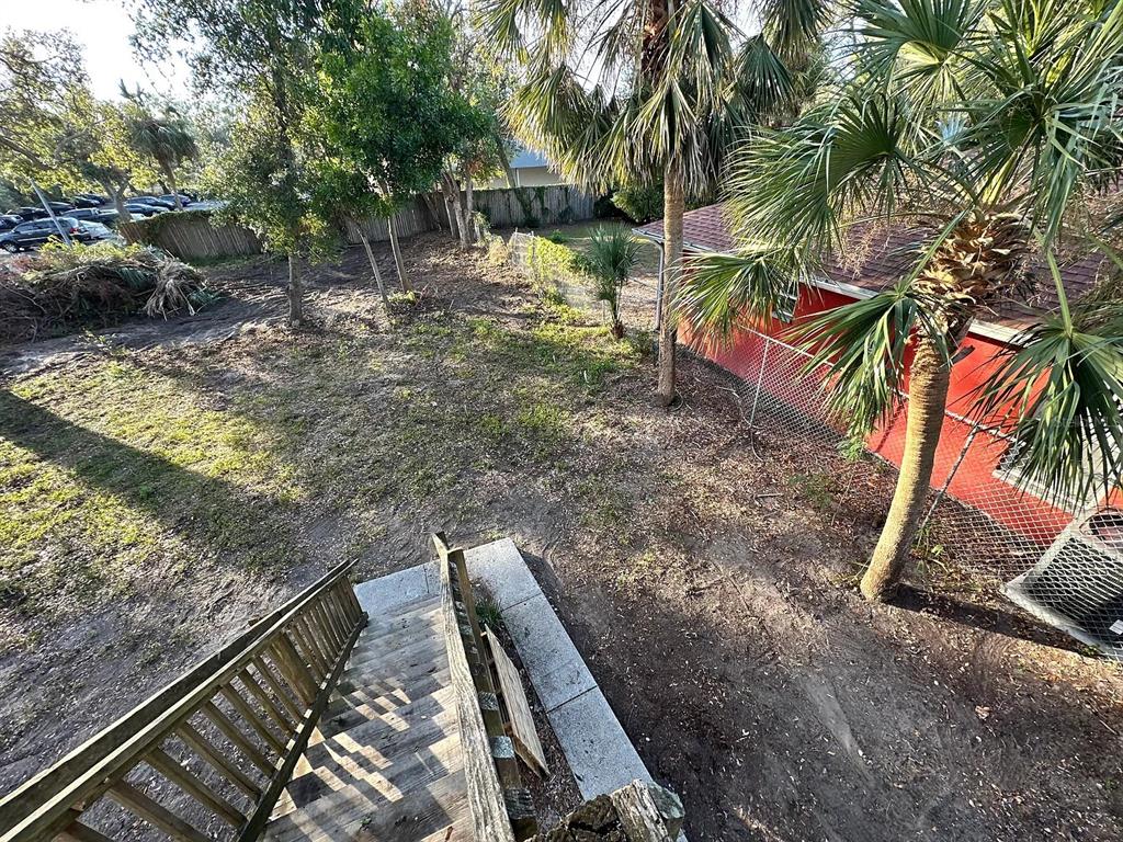 An elevated view of a backyard with a wooden staircase, dirt ground, and a red building — 1701 14TH UNIT B, ST PETERSBURG, FL