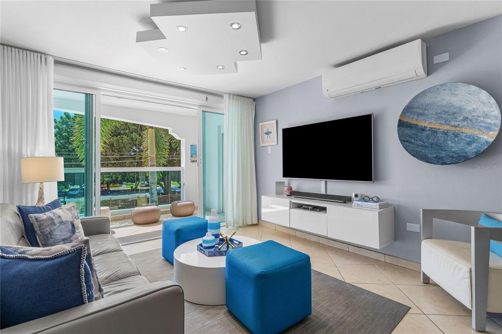 A living room features a sofa, blue ottomans, a wall-mounted television, and a balcony view — 115 ESQ CAMBIJA STREET UNIT 2B, RINCON, PR