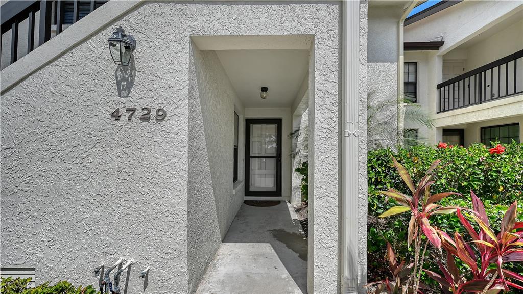 The exterior entrance of a residential unit features a concrete walkway and a storm door — 4729 WINSLOW BEACON UNIT 11, SARASOTA, FL
