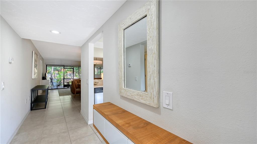 A hallway features a wooden console table, a framed mirror, and tile flooring — 4729 WINSLOW BEACON UNIT 11, SARASOTA, FL