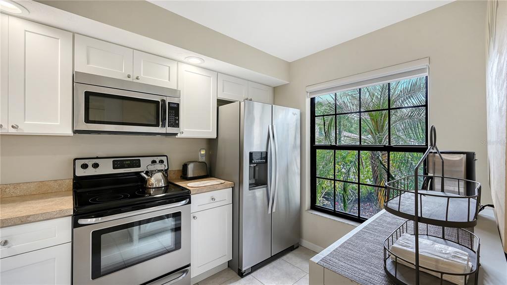 A kitchen features white cabinets, stainless steel appliances, a window, and a tiered serving tray — 4729 WINSLOW BEACON UNIT 11, SARASOTA, FL