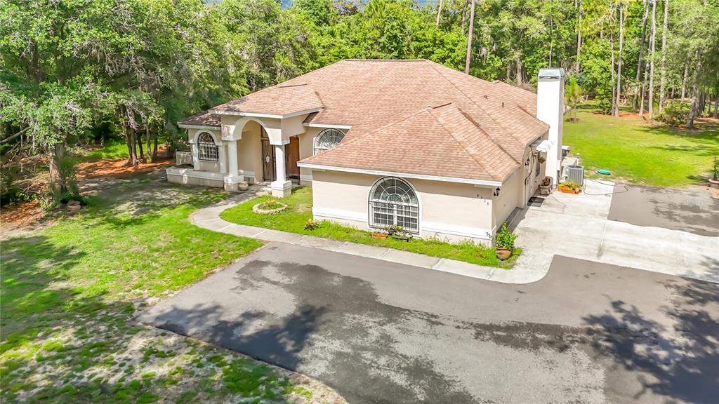 An aerial view of a single-story beige house with a brown shingled roof and driveway — 8338 HANDCART ROAD, WESLEY CHAPEL, FL