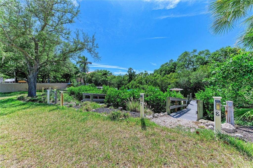 A grassy yard leads to a wooden dock surrounded by lush trees and vegetation — 347 BAYSHORE DRIVE, OSPREY, FL