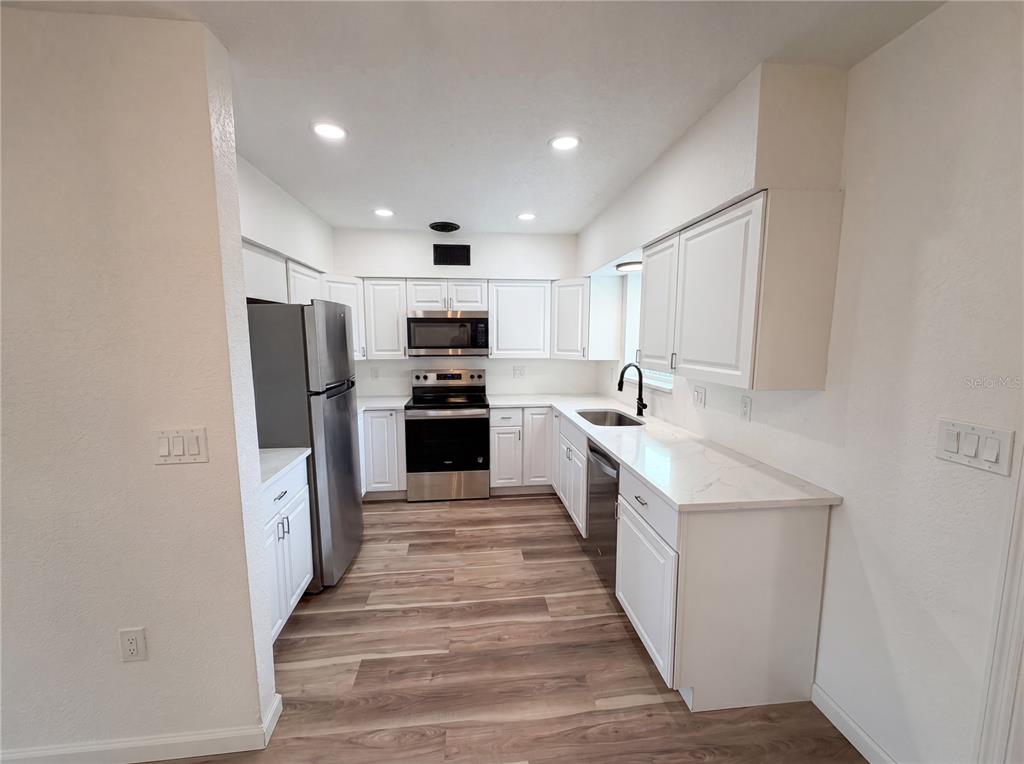 A kitchen with white cabinets, stainless steel appliances, and wood-look flooring — 567 BAYWOOD DRIVE N, DUNEDIN, FL