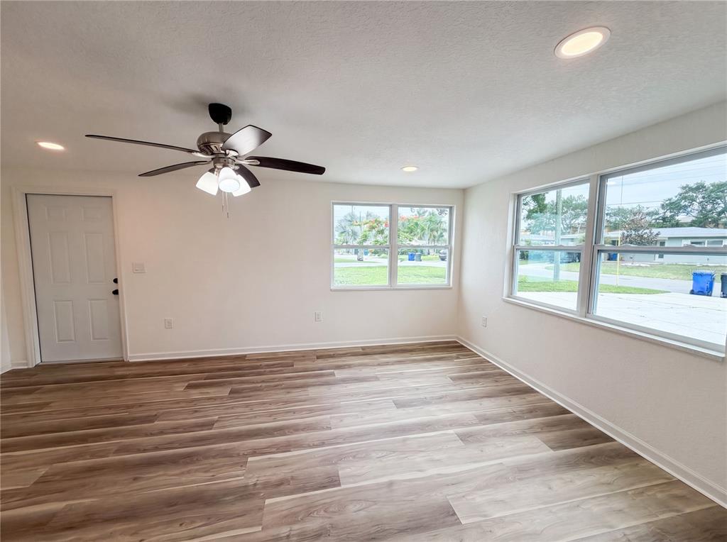 An empty room features light wood-look flooring, a ceiling fan, and large windows — 567 BAYWOOD DRIVE N, DUNEDIN, FL