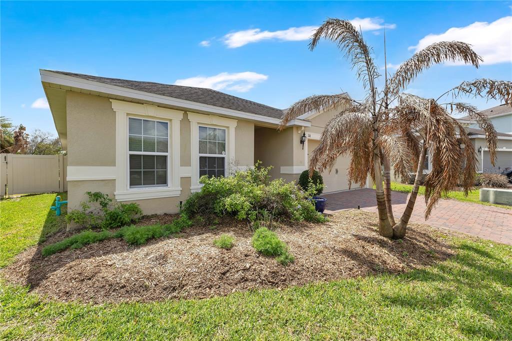 A single-story house with a tan stucco exterior, a brick driveway, and a palm tree — 116 WHIRLAWAY DRIVE, DAVENPORT, FL
